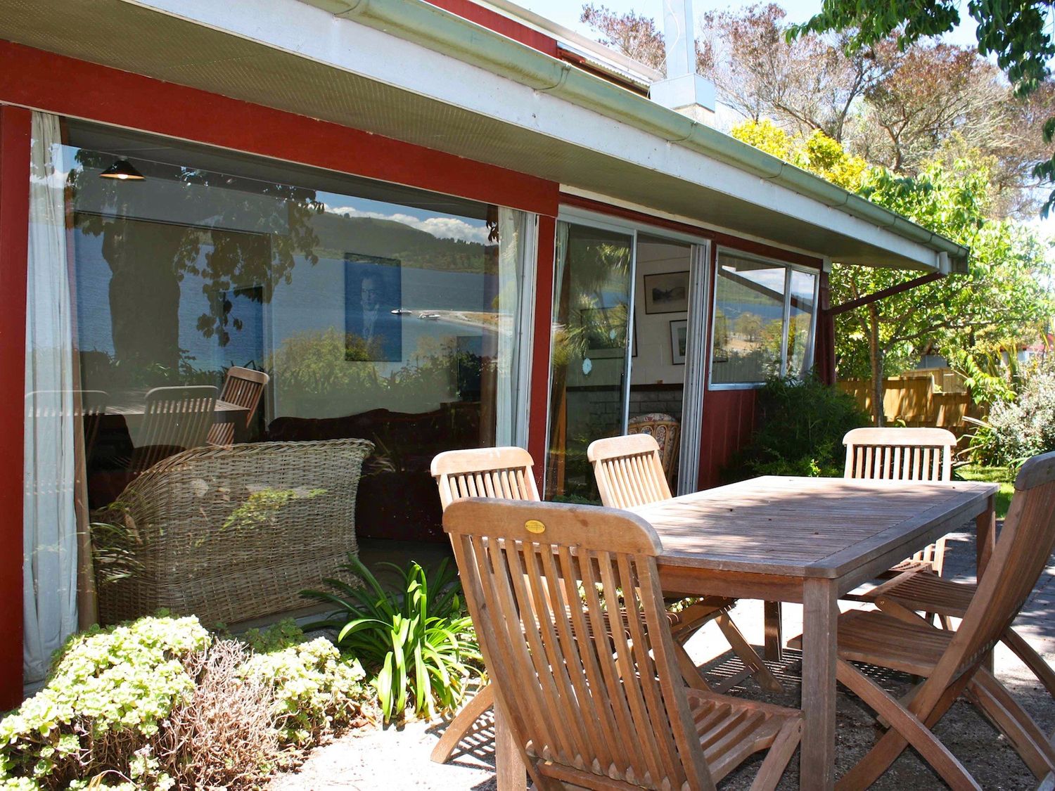 An outdoor patio area with a wooden table and chairs next to a house with large windows at Moeroa - Wharewaka Holiday Home in Wharewaka