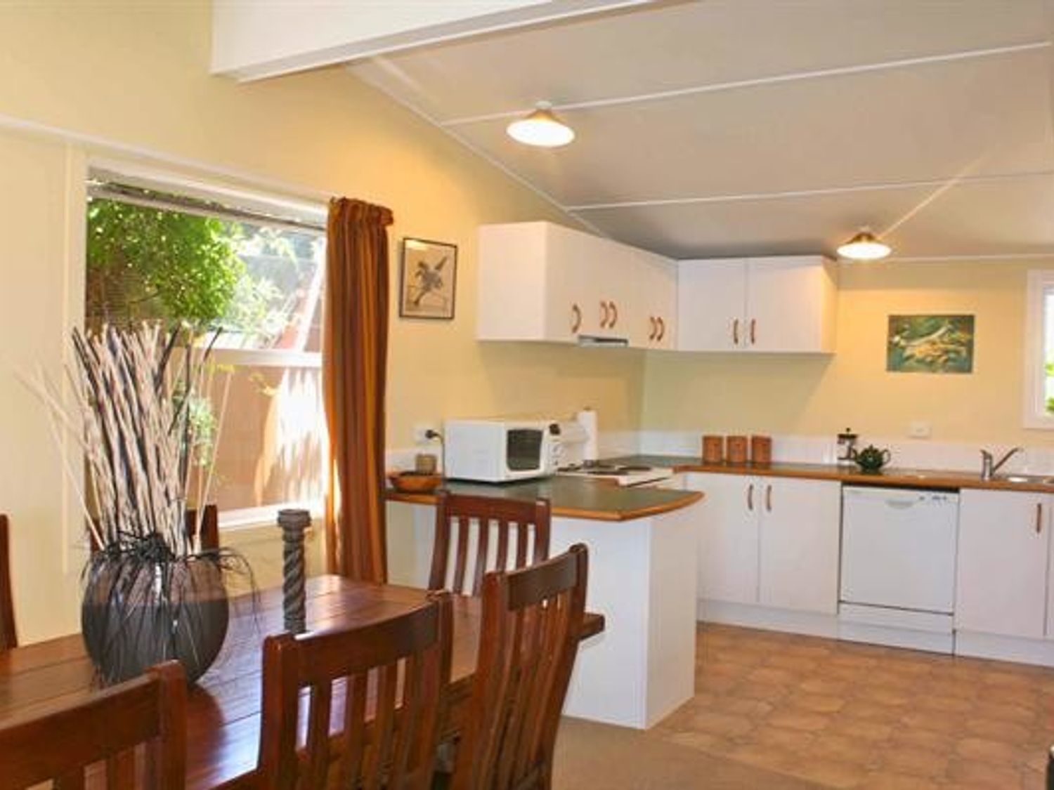 A kitchen and dining area with a wooden dining table and chairs white cabinets and a microwave at Moeroa - Wharewaka Holiday Home in Wharewaka