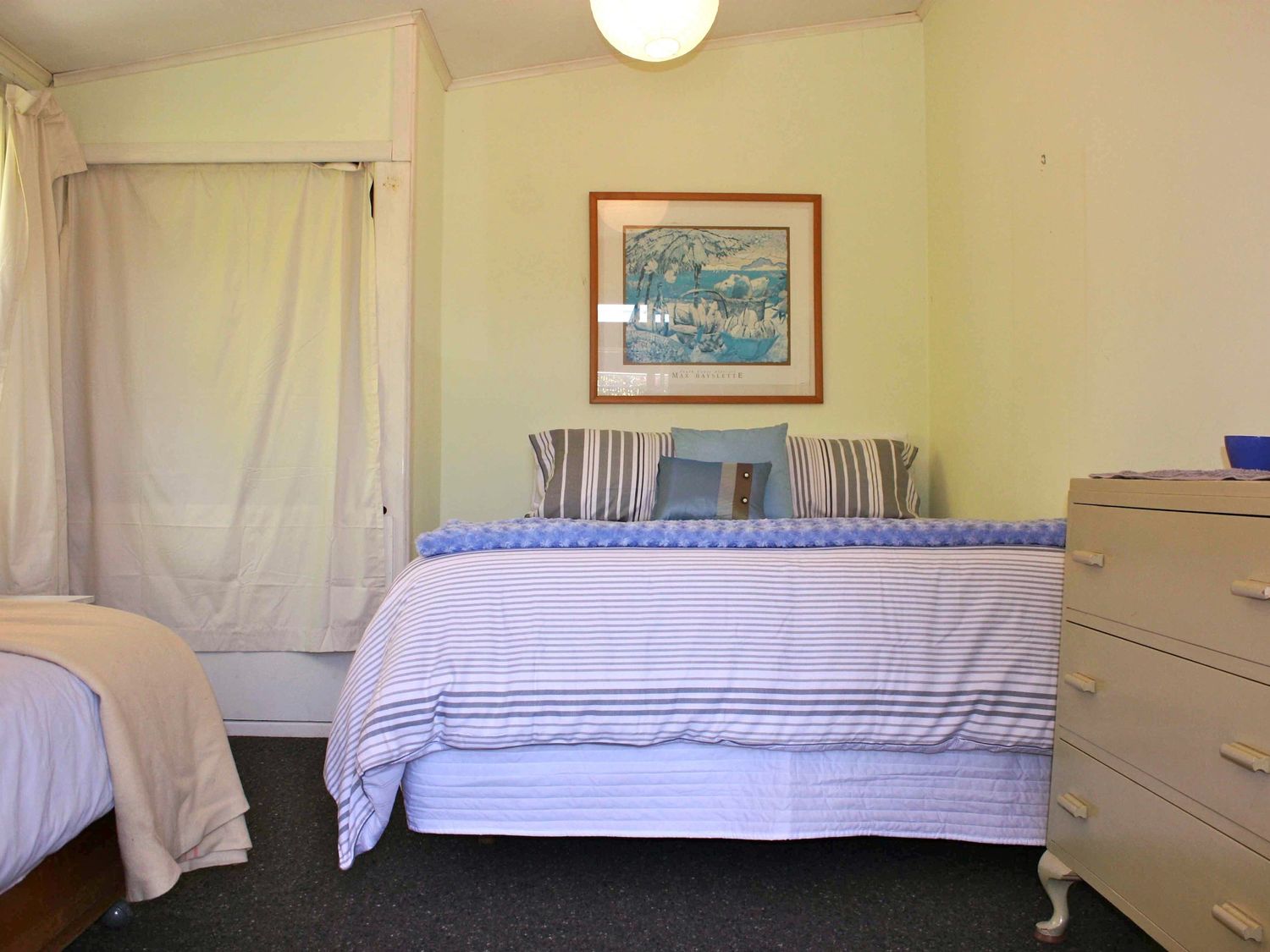 A bedroom with a bed with striped bedding pillows a dresser and a curtain on the window at Moeroa - Wharewaka Holiday Home in Wharewaka