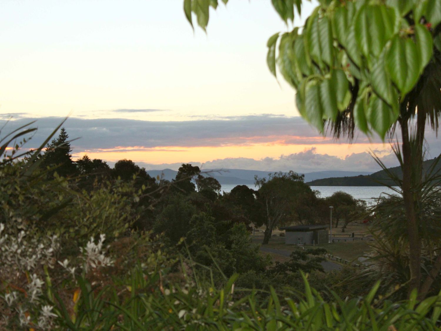 A view of trees water and hills at sunset at Moeroa - Wharewaka Holiday Home in Wharewaka