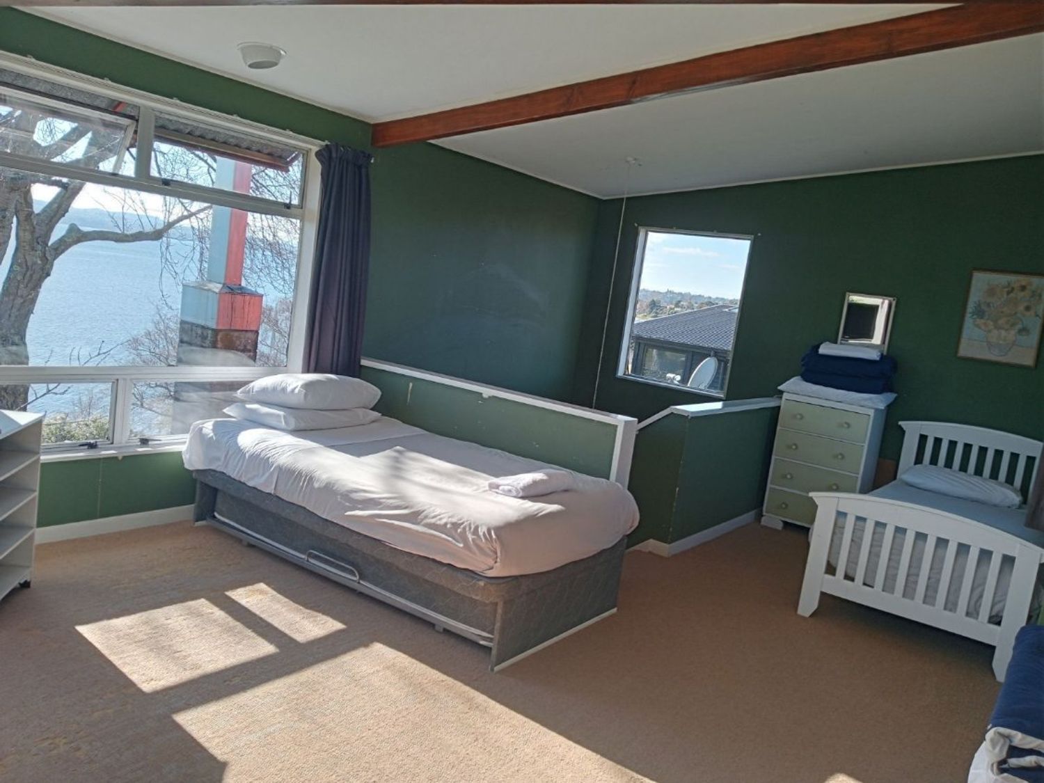 A bedroom with two beds a dresser and windows showing a lake at Moeroa - Wharewaka Holiday Home in Wharewaka