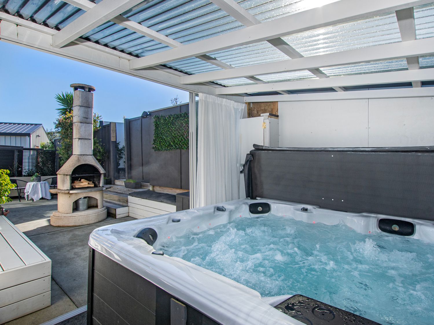 An outdoor space with a hot tub and fireplace at Sunnyside Spa Retreat - Mangawhai Heads