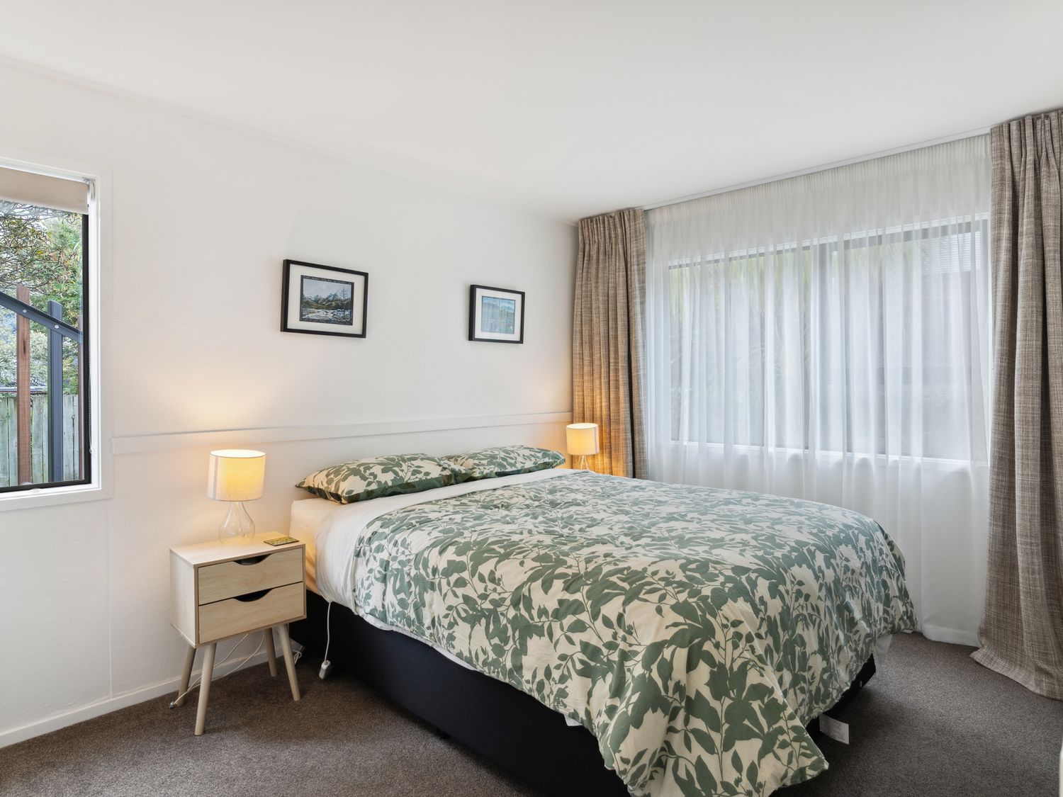 A bedroom with a double bed bedside tables with lamps two framed pictures on the wall and windows with curtains at Central Southern Lakes - Queenstown Holiday Home in Queenstown