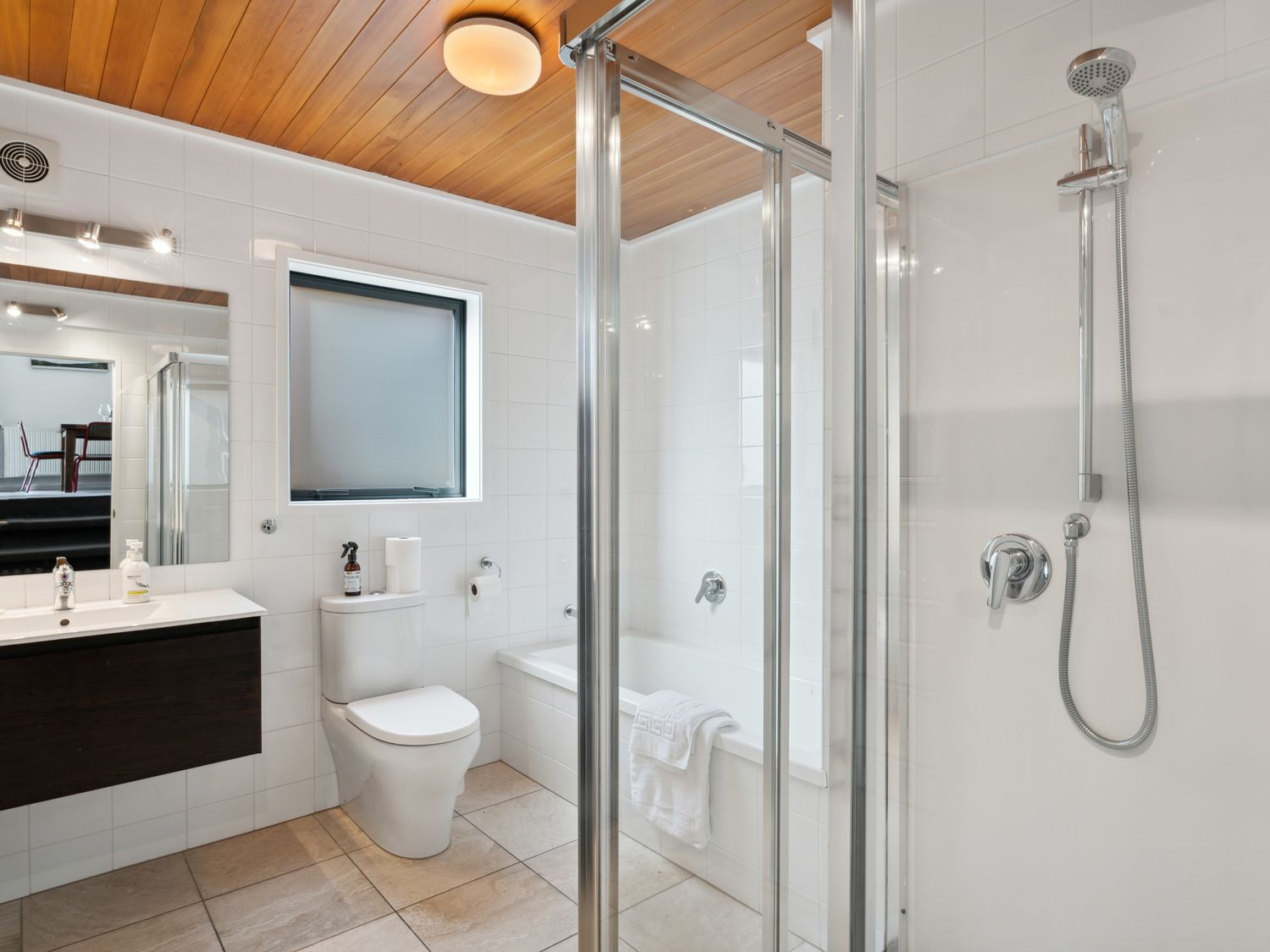 A bathroom with a toilet, a bathtub with a towel, a shower area, and a vanity with a mirror and sink at Central Southern Lakes - Queenstown Holiday Home in Queenstown