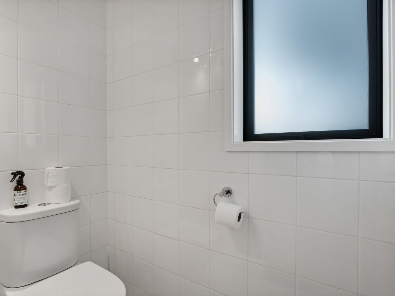 A white tiled bathroom with a toilet two rolls of toilet paper and a frosted window at Central Southern Lakes Queenstown Holiday Home in Queenstown