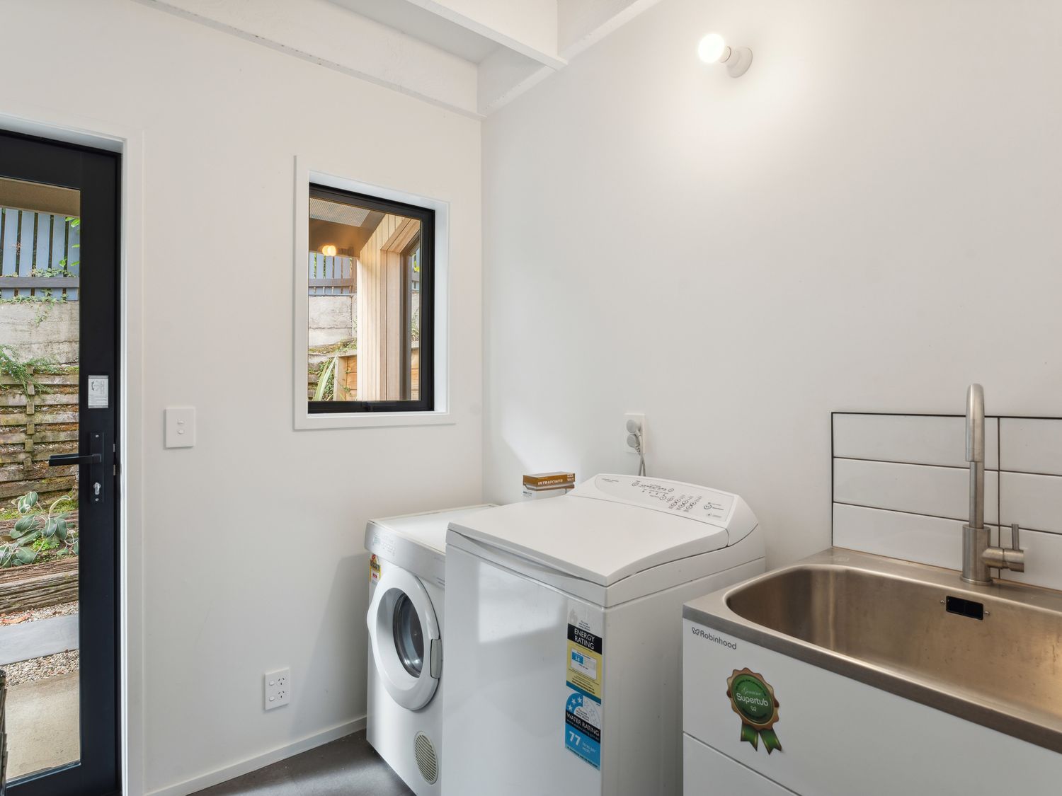 A laundry room with a washing machine dryer and a sink next to a window and a door at Central Southern Lakes Queenstown Holiday Home Queenstown