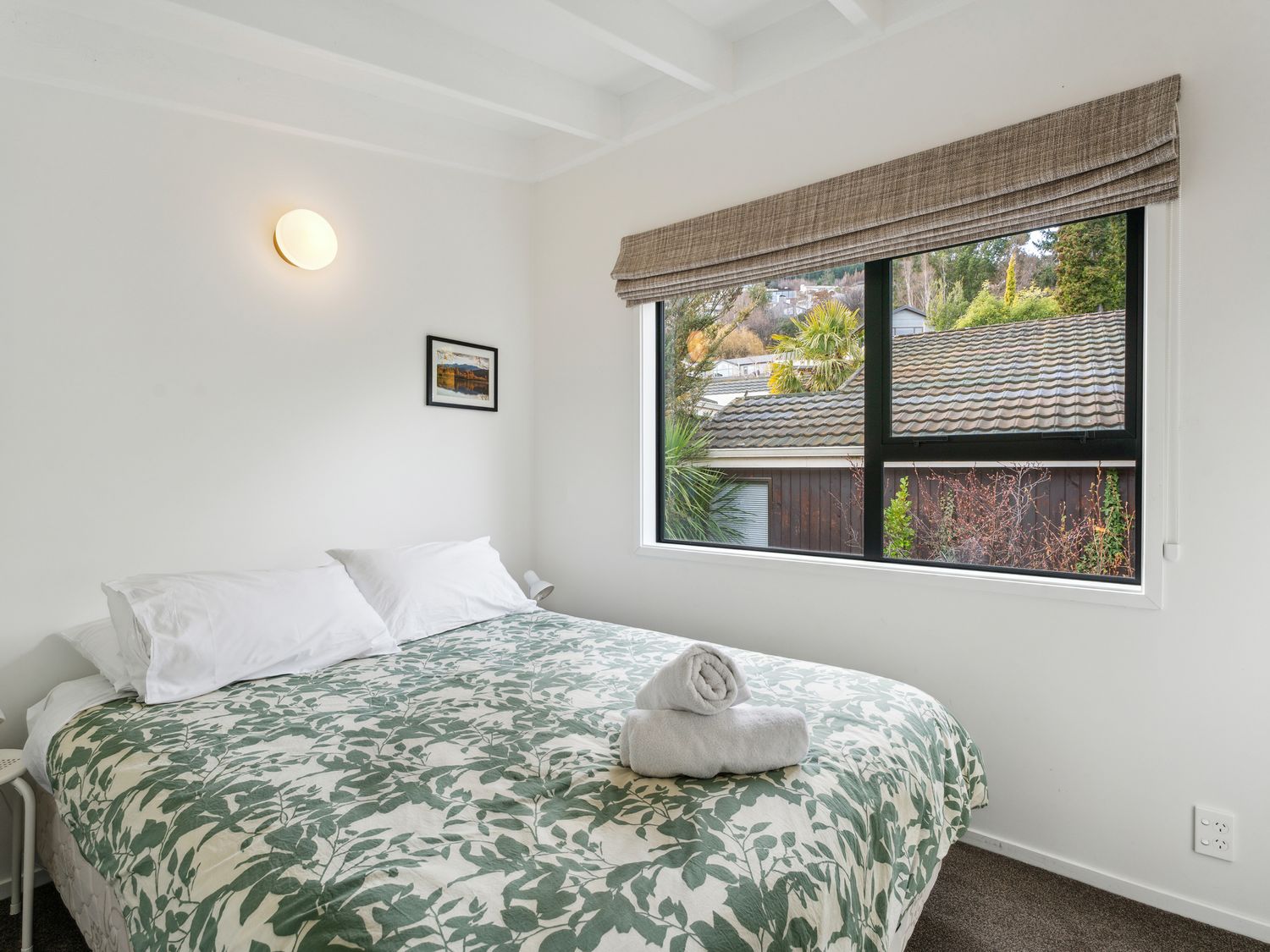 A bedroom with a bed with patterned bedding and two pillows beside a window with a view at Central Southern Lakes - Queenstown Holiday Home in Queenstown