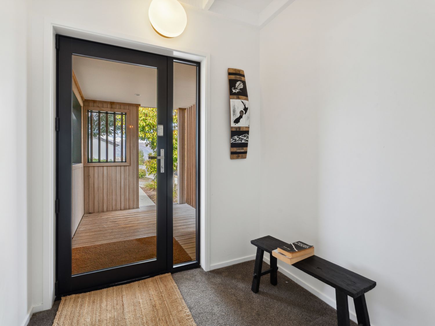 An entryway with glass double doors a black bench with books on it and a wooden wall decoration at Central Southern Lakes - Queenstown Holiday Home in Queenstown