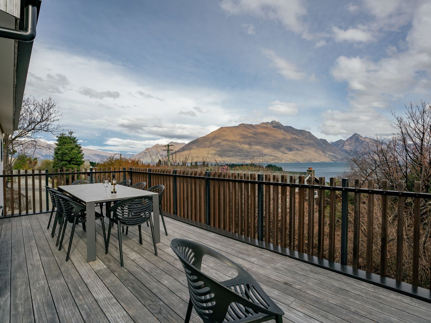 An outdoor deck with a dining table and chairs overlooking mountains and a lake at Central Southern Lakes - Queenstown Holiday Home in Queenstown