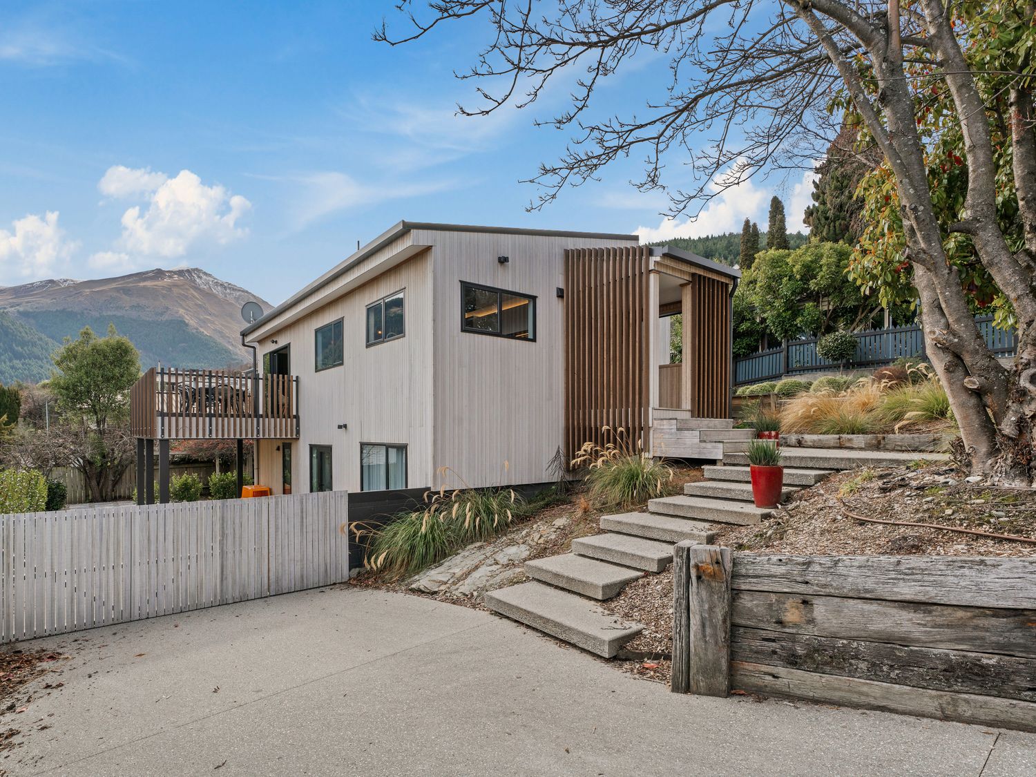 A modern two-story house with a deck and stairs surrounded by trees and plants at Central Southern Lakes Queenstown