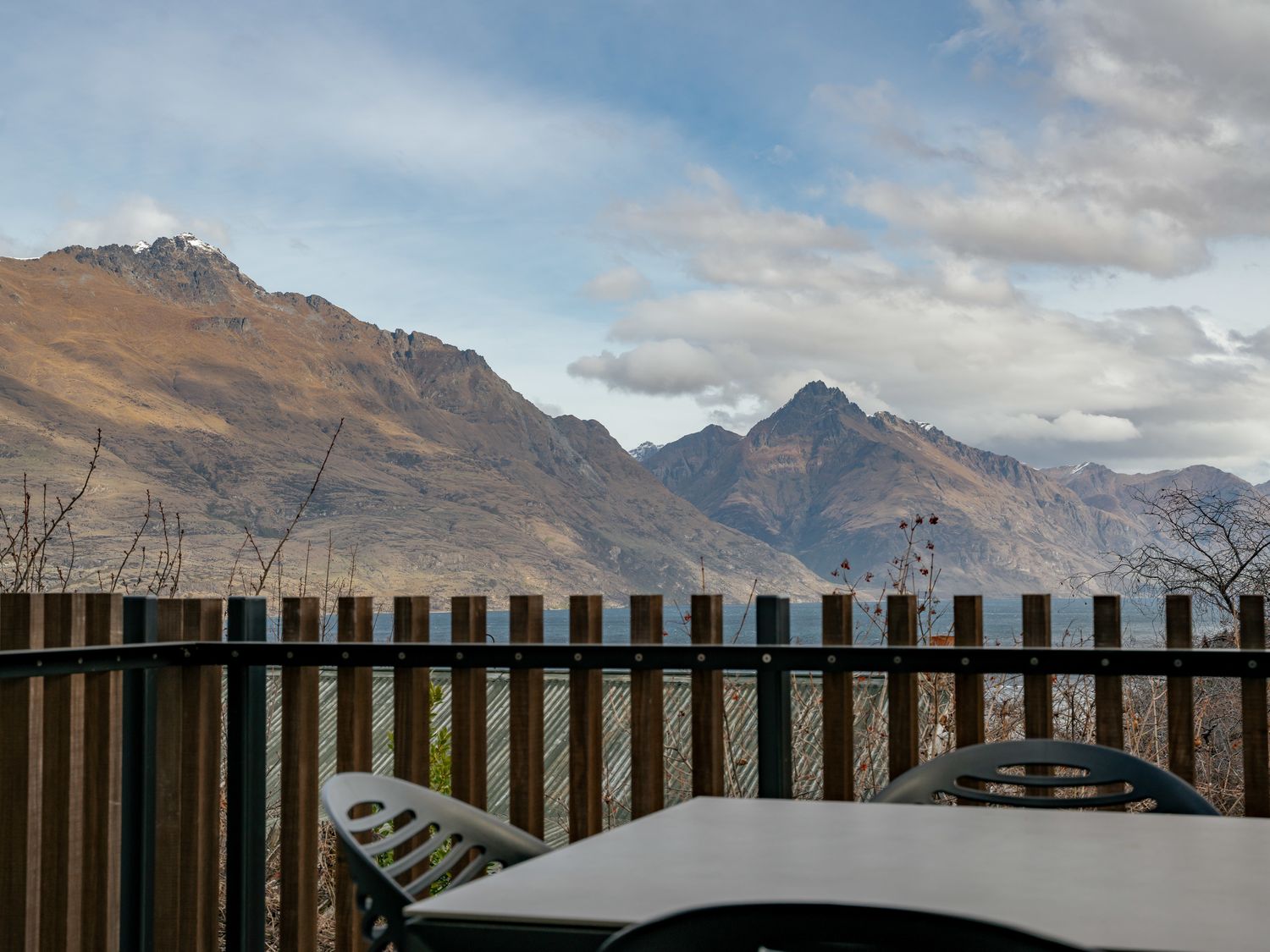 A balcony with a table and chairs overlooking mountains and a lake at Central Southern Lakes - Queenstown Holiday Home in Queenstown