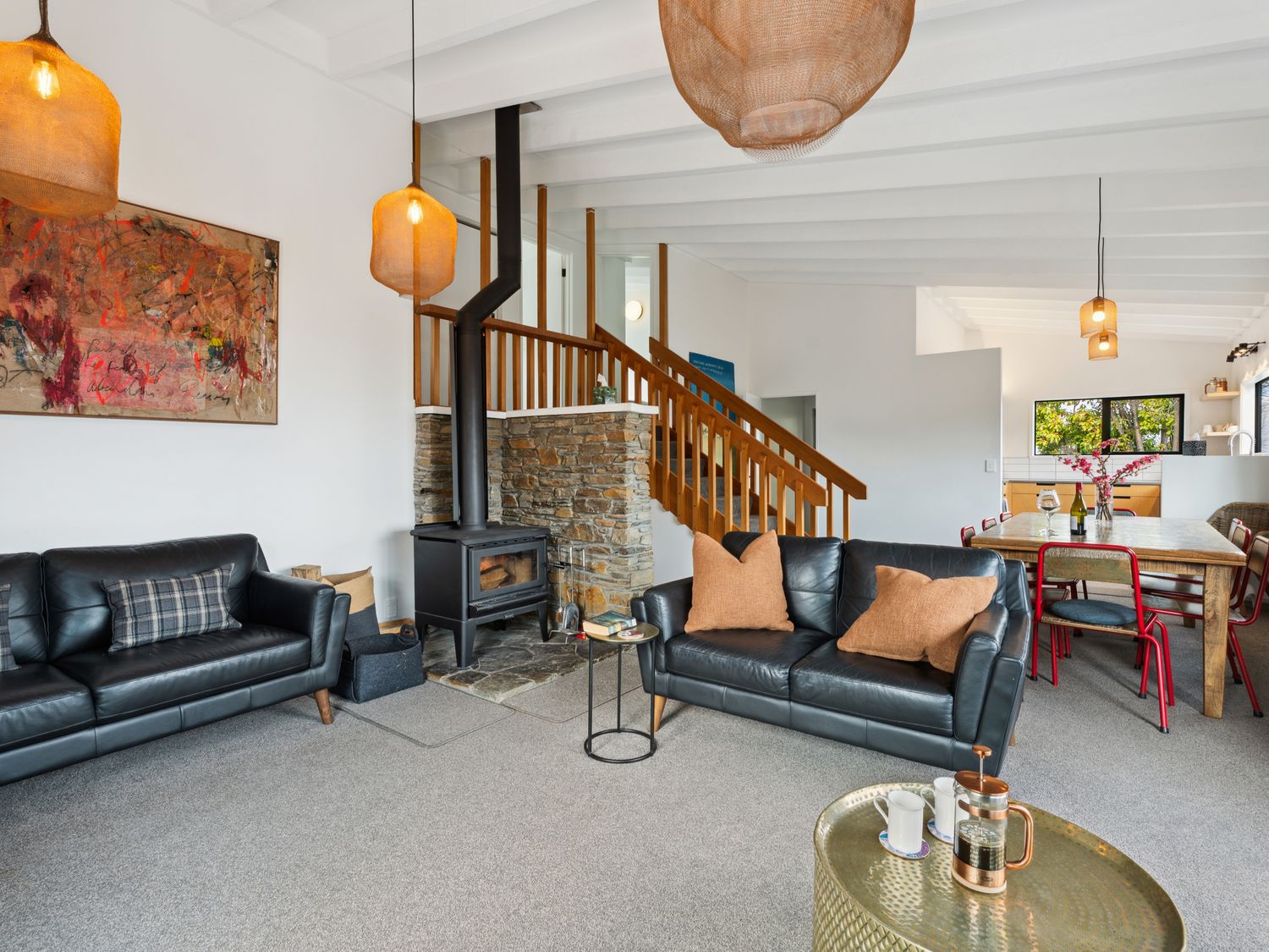 A living room with black leather sofas a wood stove and a dining table with red chairs at Central Southern Lakes - Queenstown Holiday Home in Queenstown