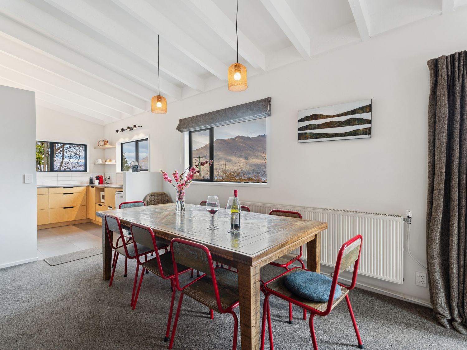 A dining area with a wooden table and red chairs next to a kitchen with wooden cabinets at Central Southern Lakes Queenstown Holiday Home in Queenstown
