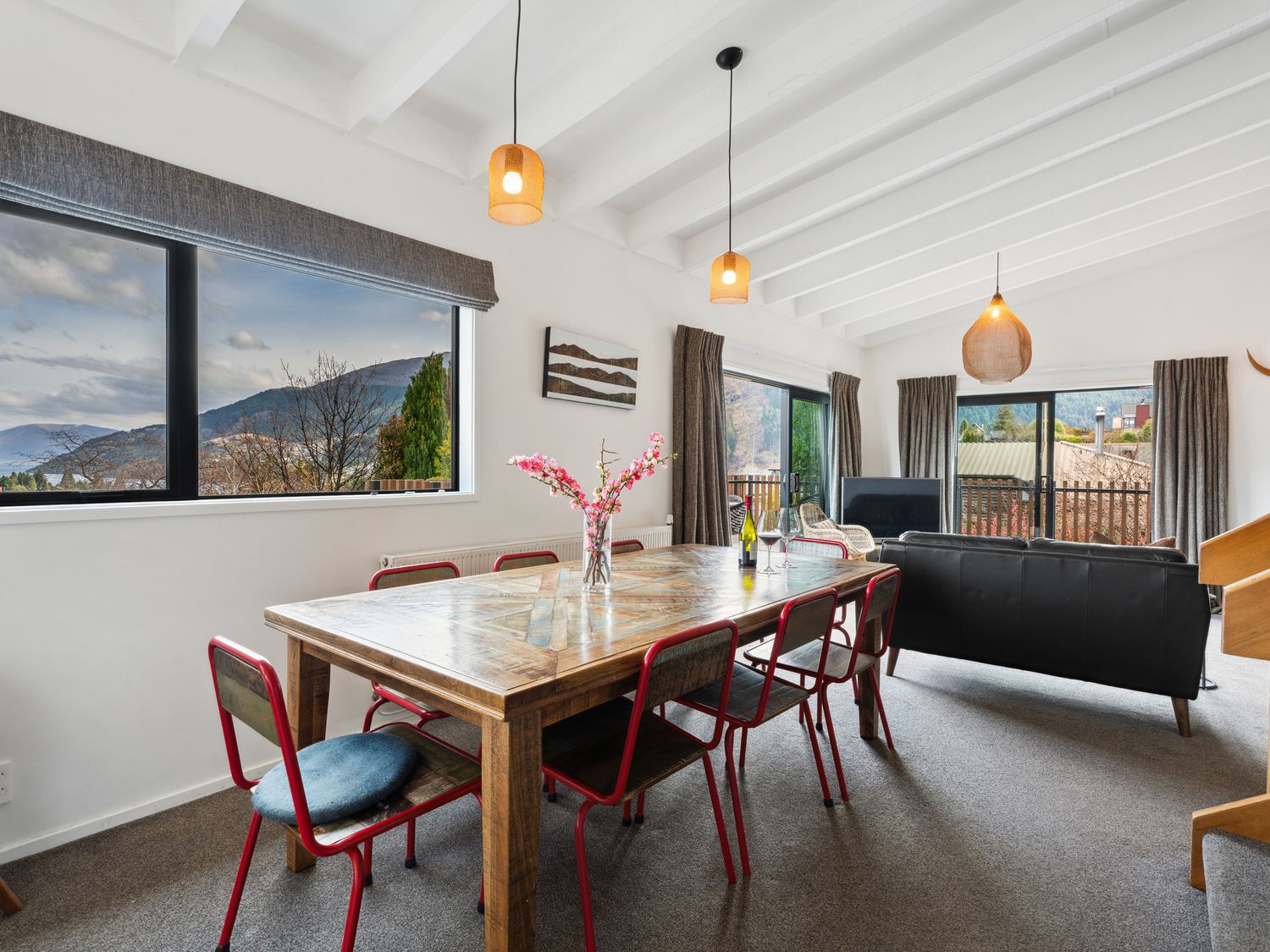 A dining area with a wooden table and red chairs next to a living room with a black sofa and television at Central Southern Lakes Queenstown Holiday Home Queenstown