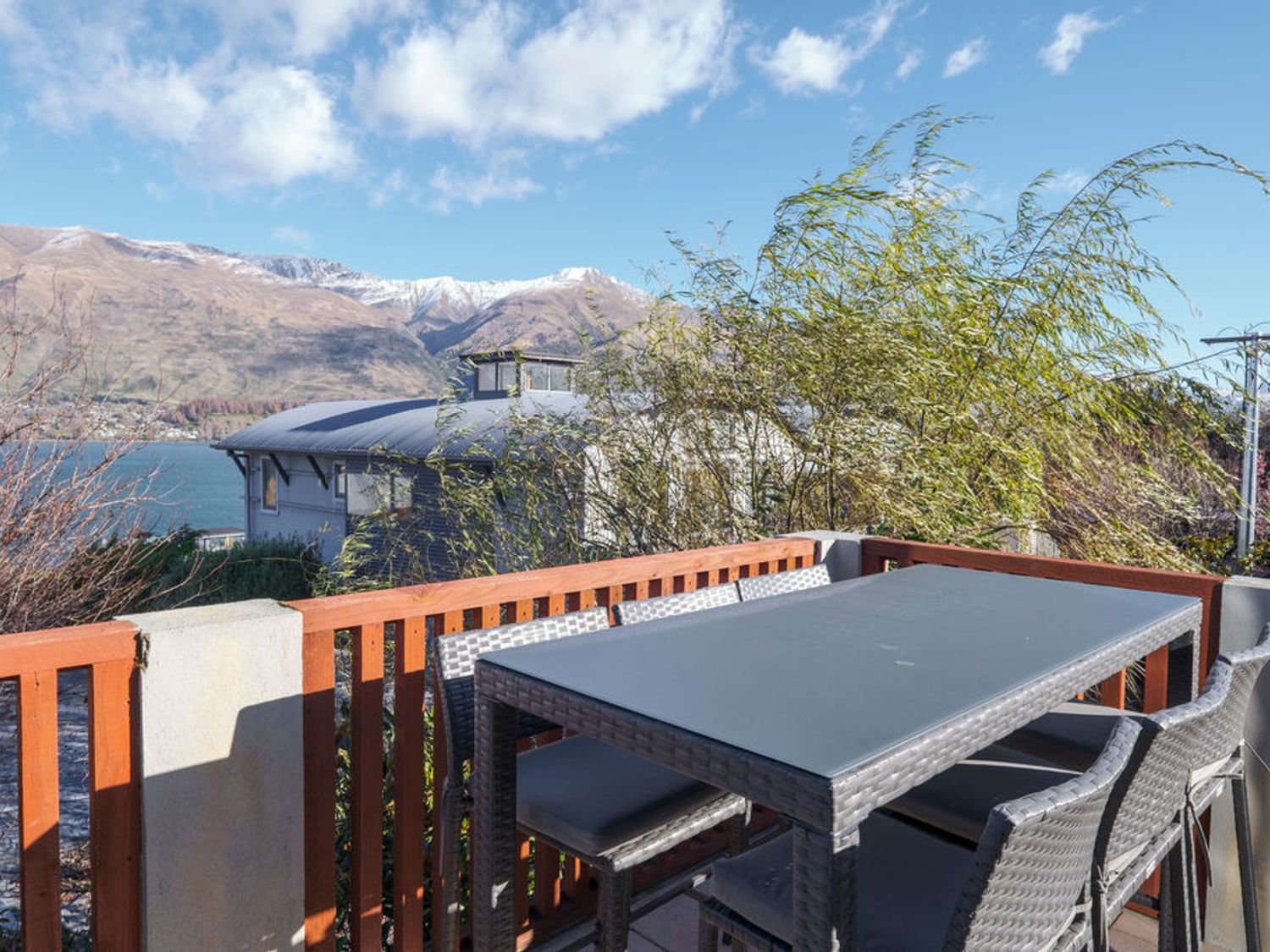 An outdoor dining table with chairs on a balcony overlooking a lake and mountains at Lakeview Heights - Wanaka Home - Bachcare NZ in Wanaka