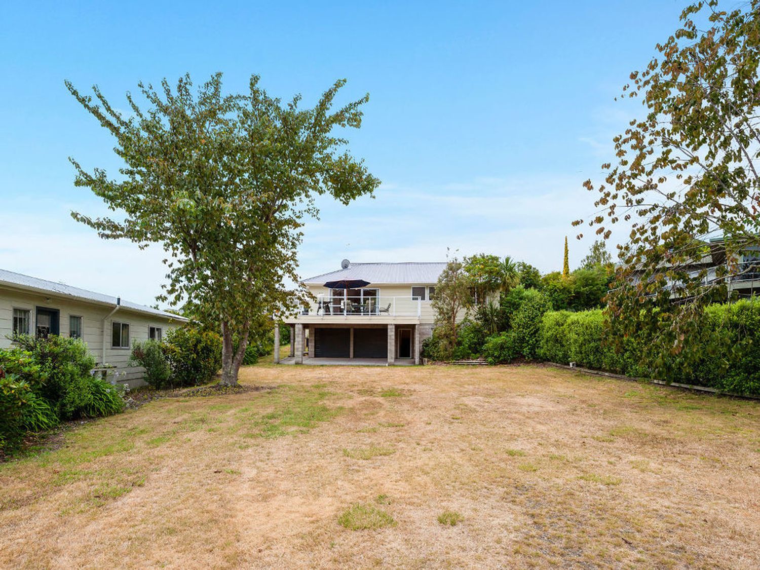 A house with a deck and umbrella in a backyard with trees and grass at Kinloch Family Retreat in Acacia Bay
