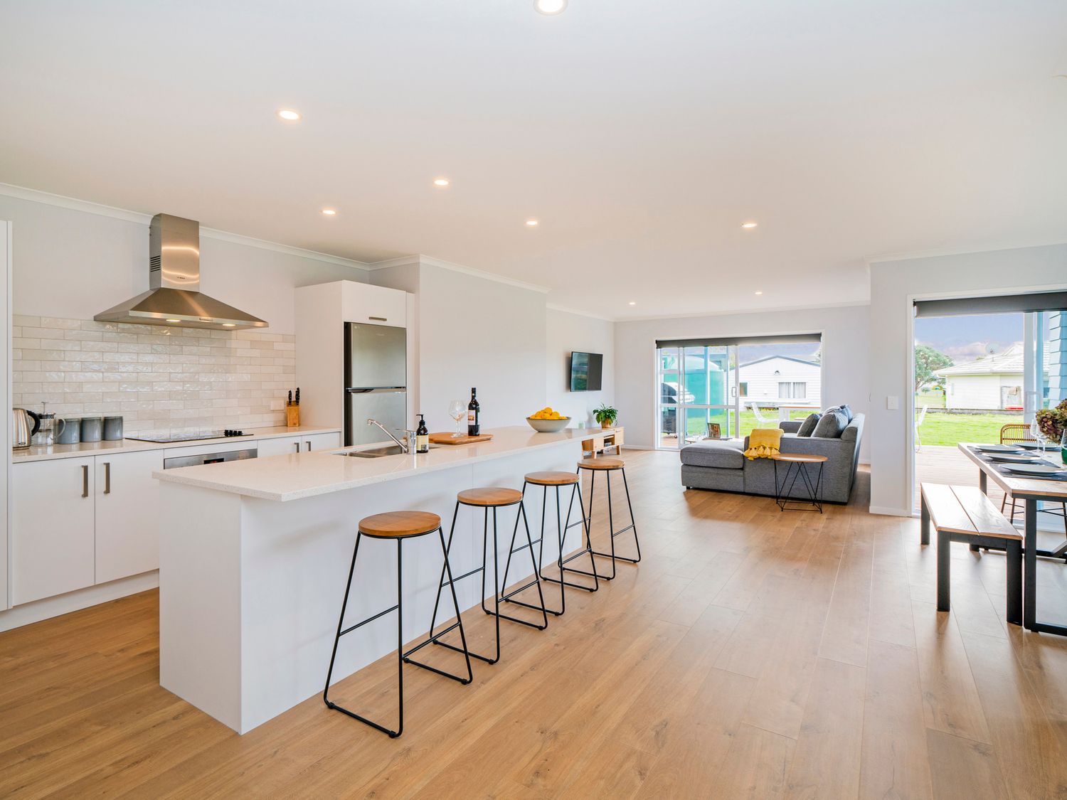 An open kitchen and living area with a kitchen island and bar stools at Seascape - Cooks Beach Holiday Home in Cooks Beach