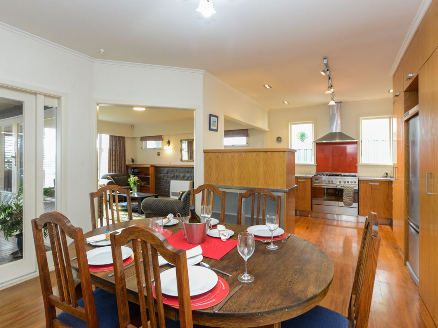 A dining area with a wooden table set for six near a kitchen with wooden cabinets and stainless steel appliances at Breakwater Cottage - Napier Holiday Home in Bluff Hill