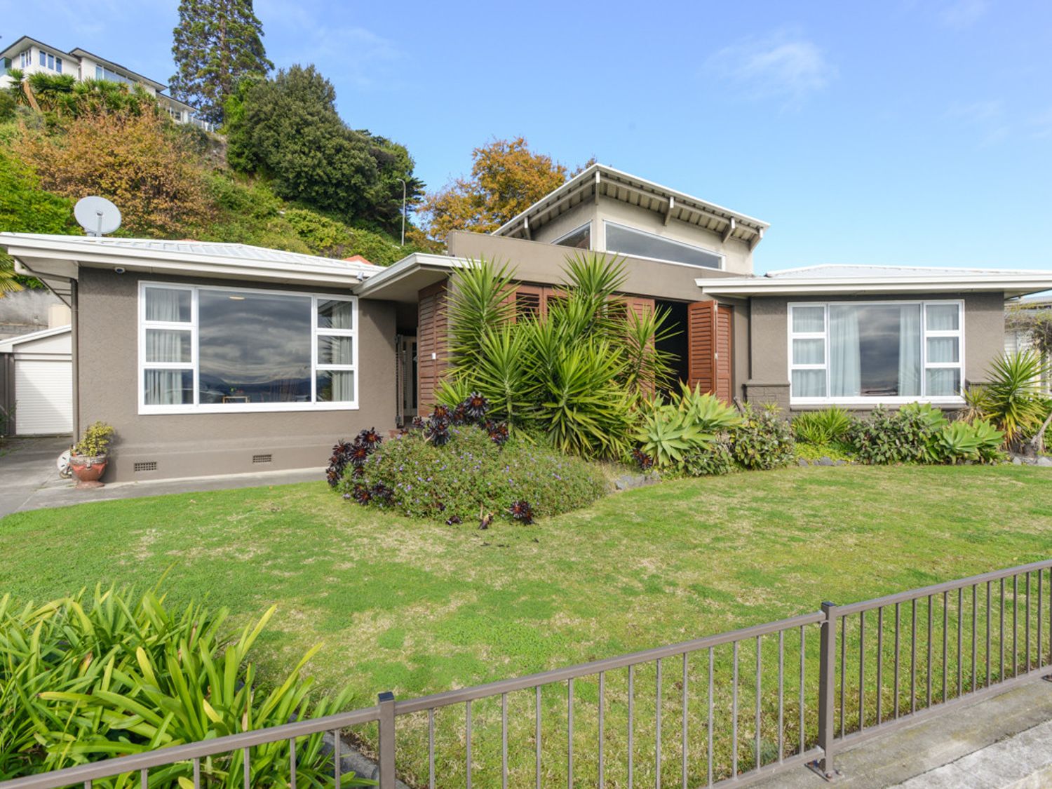 A front view of a single-story house with large windows and a garden with plants at Breakwater Cottage - Napier Holiday Home Bluff Hill