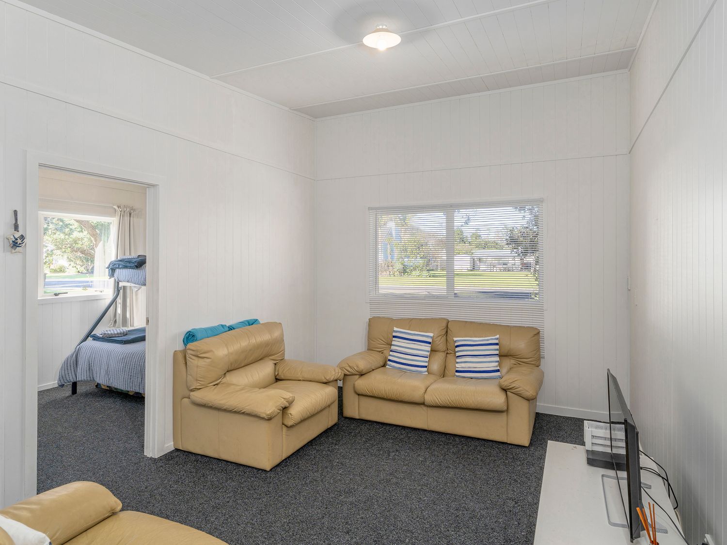 A living room with beige sofas striped pillows and a television at Rangimarie on Kenwood- Matarangi Holiday Home in Matarangi