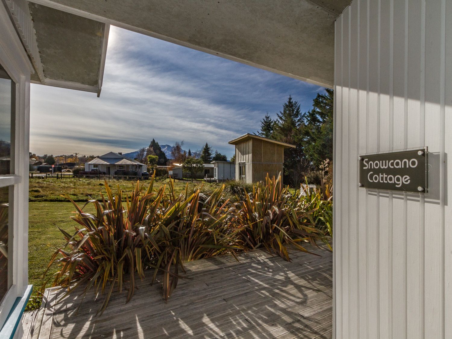 A porch with plants and a view of houses and mountains at Snowcano Cottage in Rangataua