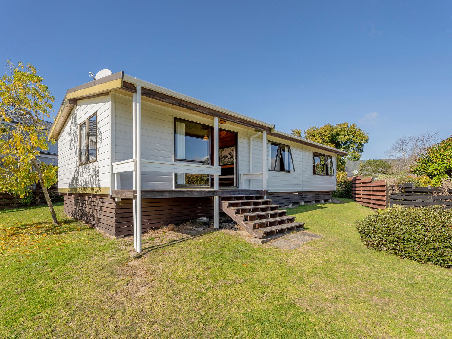 A single story house with a small porch and stairs on a grassy lawn at Retro Revival - Pauanui Holiday Home in Pauanui