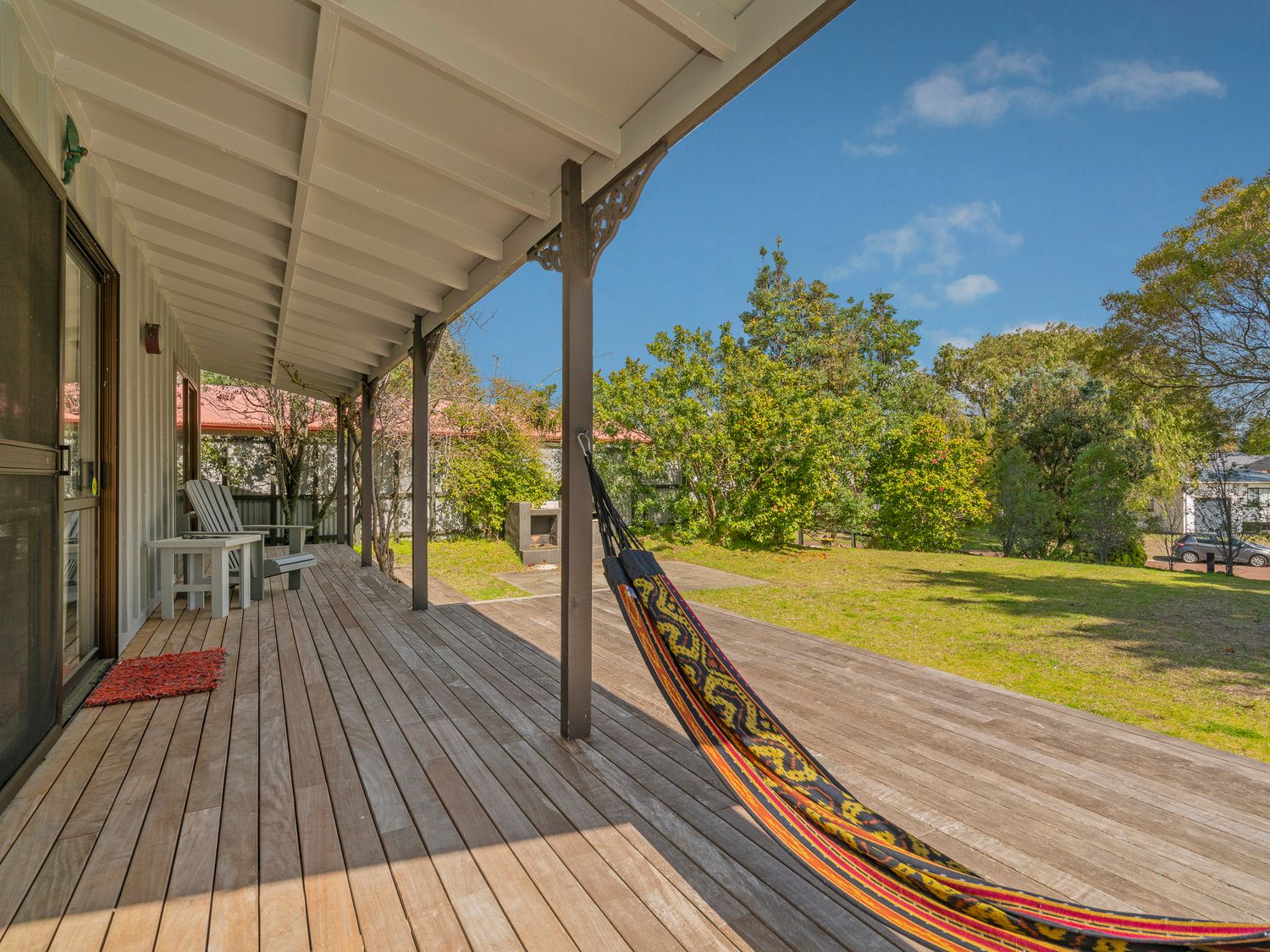A wooden deck with a covered porch patio chairs a colorful hammock and a grassy yard at Jewel on Crown Reef in Pauanui