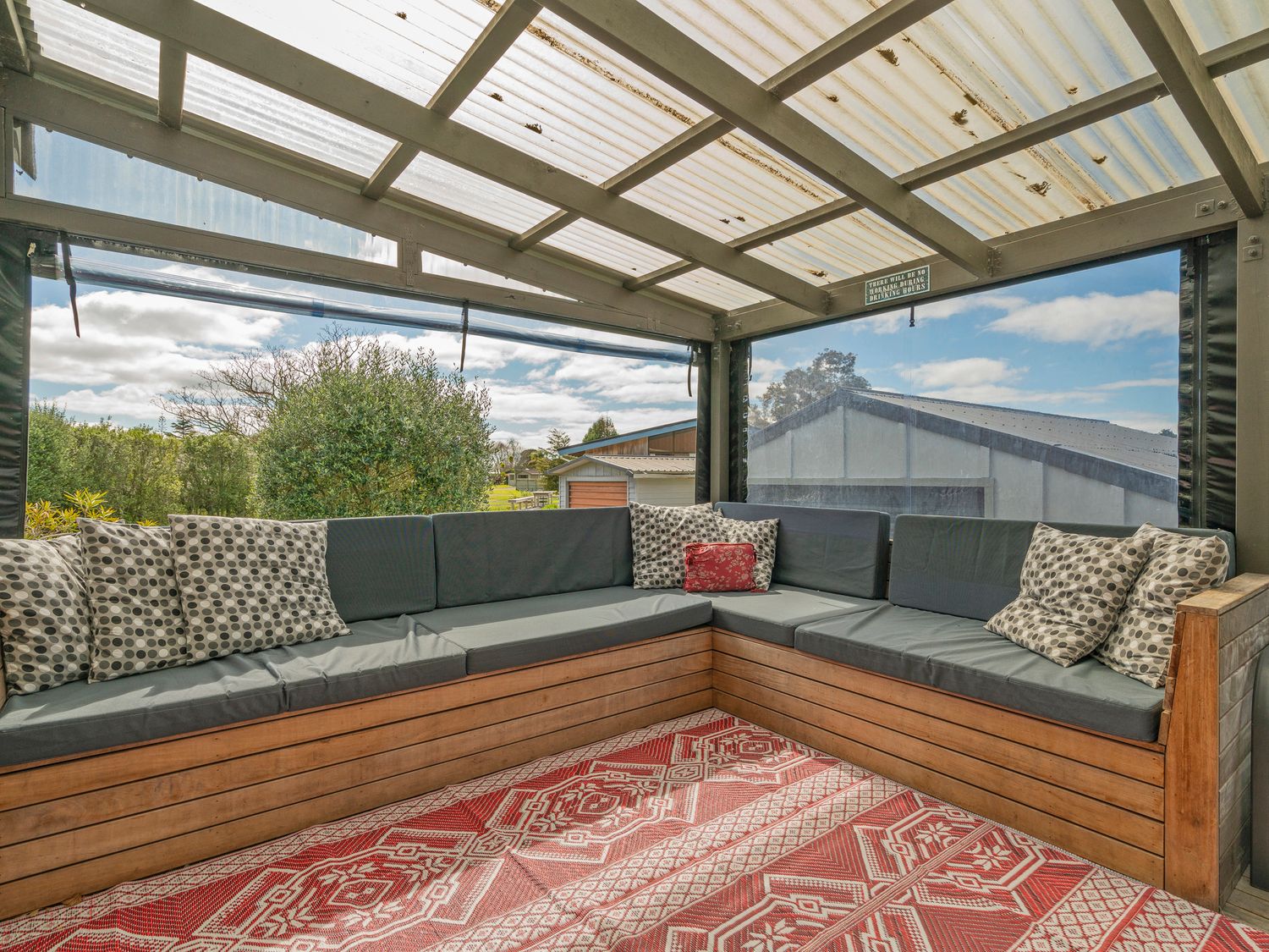 An outdoor seating area with wooden bench and grey cushions under a transparent roof at Jewel on Crown Reef - Pauanui Holiday Home in Pauanui