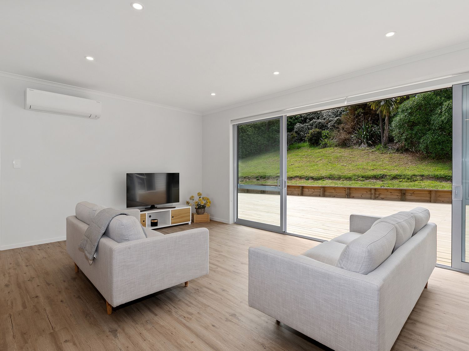 A living room with two sofas a television and large sliding glass doors showing outdoor greenery at The Platinum Rendezvous - Matapouri Holiday Home in Matapouri