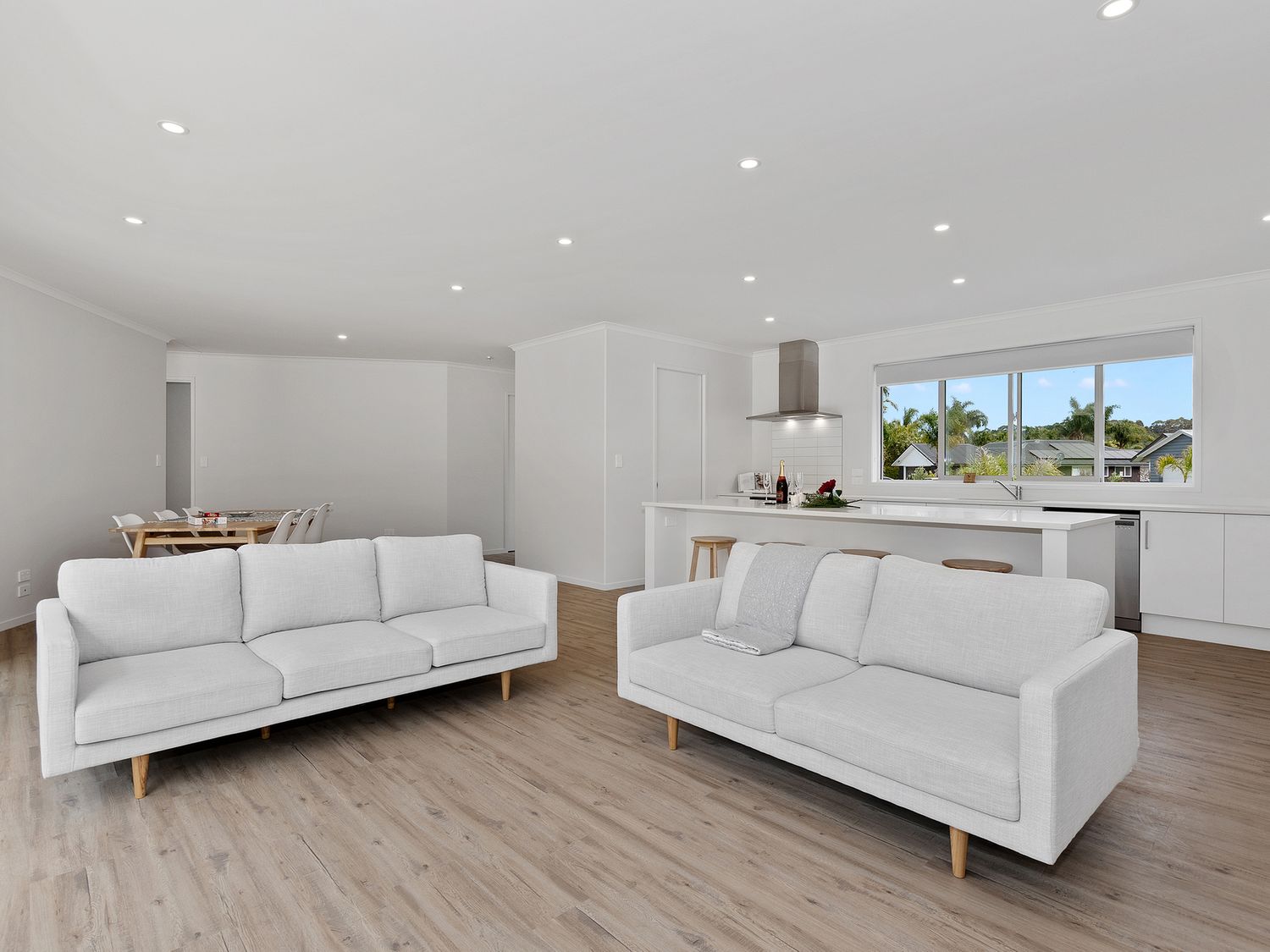 A living space with two white sofas a wooden floor a dining table with chairs and a kitchen with an island and stools at The Platinum Rendezvous - Matapouri Holiday Home in Matapouri