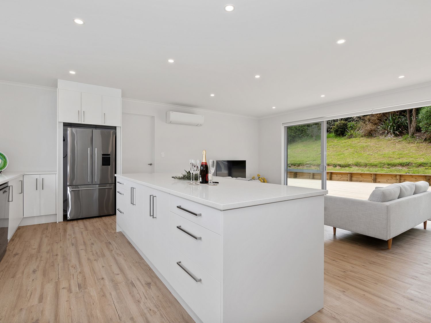 A kitchen with a large island counter next to a living area with a sofa and large sliding glass door at The Platinum Rendezvous - Matapouri Holiday Home in Matapouri