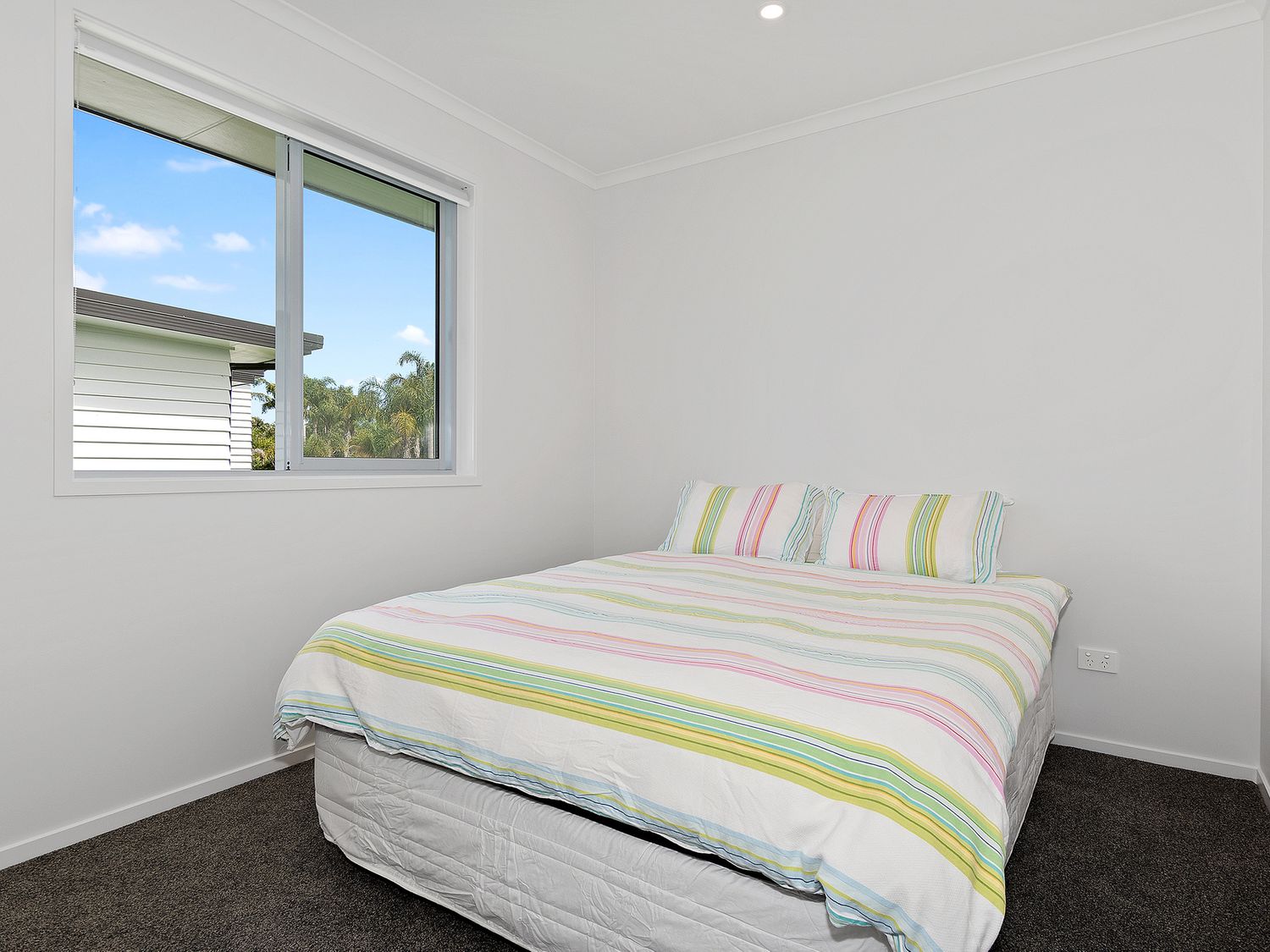A bedroom with a bed covered in striped bedding next to a window at The Platinum Rendezvous - Matapouri Holiday Home in Matapouri