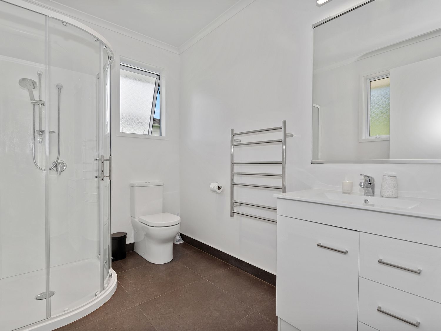 A bathroom with a shower enclosure a toilet a vanity with a sink and mirror and a towel rack at The Platinum Rendezvous - Matapouri Holiday Home in Matapouri