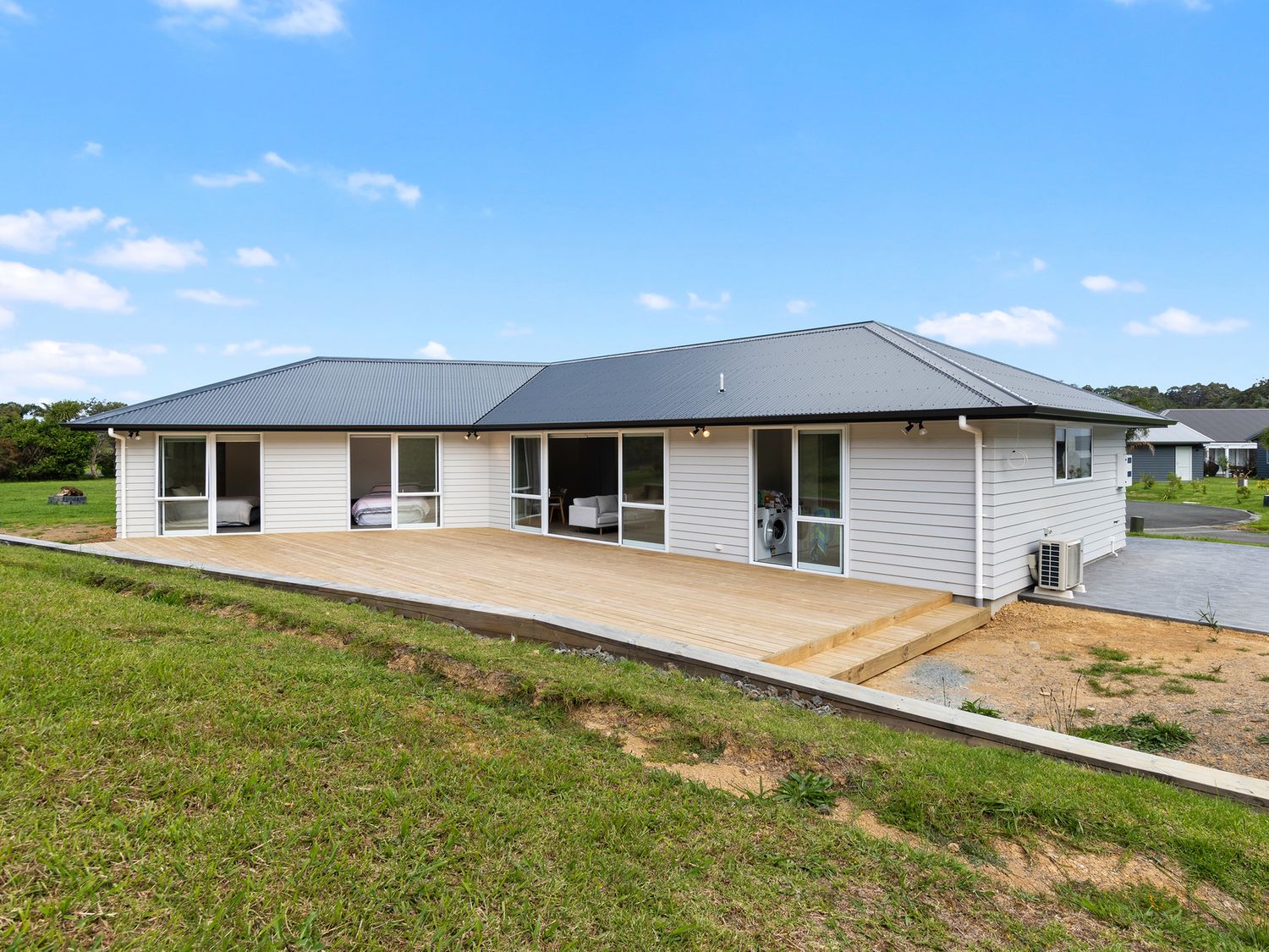 A single story house with a wide wooden deck and glass sliding doors on a grassy plot at The Platinum Rendezvous - Matapouri Holiday Home in Matapouri
