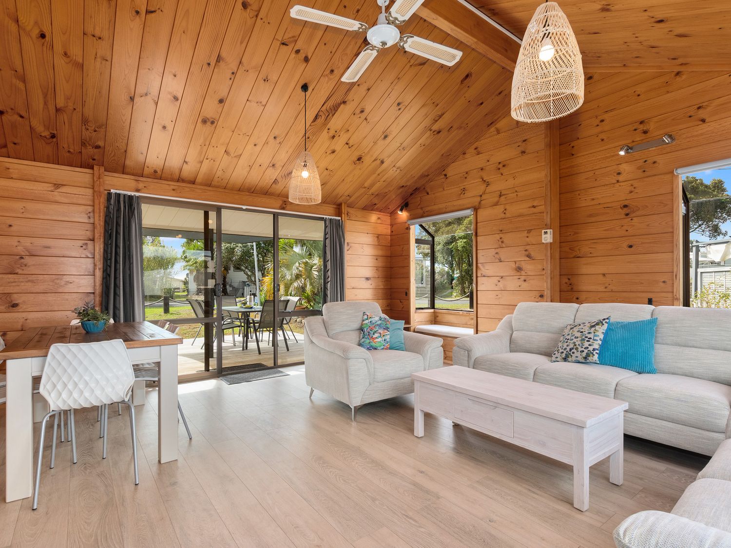 A wooden living room with a sofa armchair coffee table dining table and sliding glass doors at Bream Bay Sands - Ruakaka Holiday Home in Ruakaka