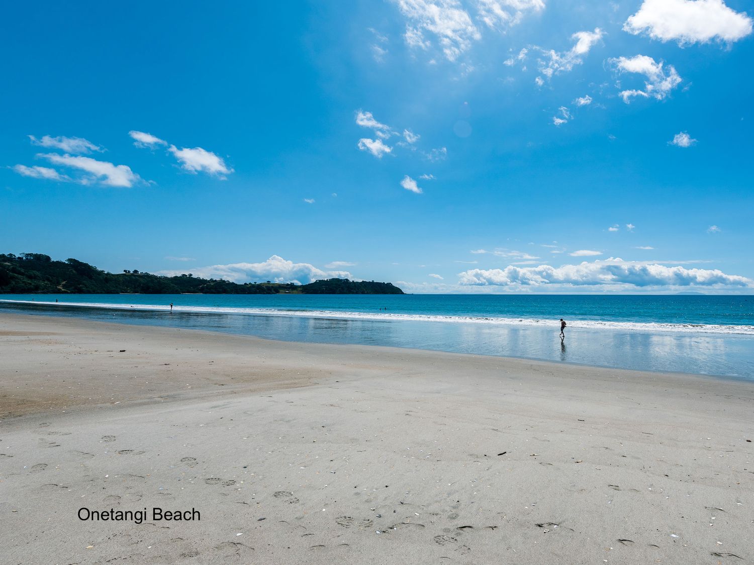 A sandy beach with a few people near the shore and a partly cloudy sky at Eden Escape Onetangi in Onetangi