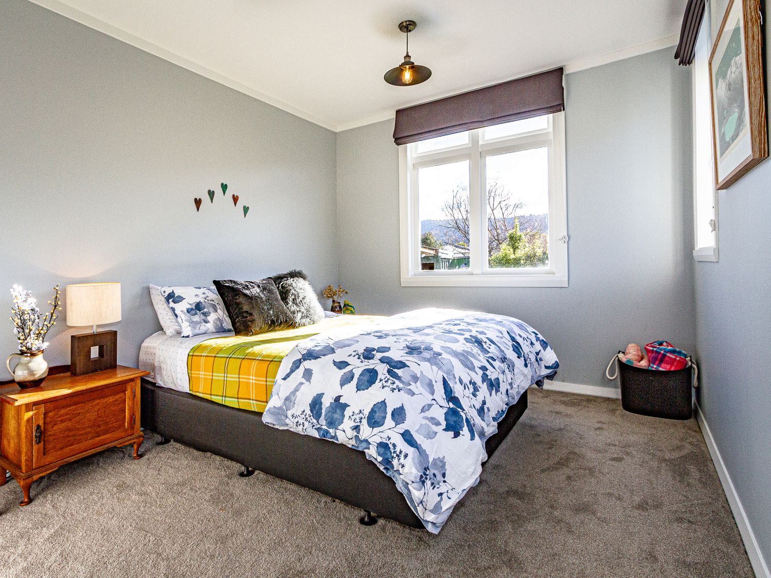 A bedroom with a bed covered with floral and plaid bedding and a wooden nightstand with a lamp at Ohakune Barracks - Ohakune Holiday Home in Ohakune