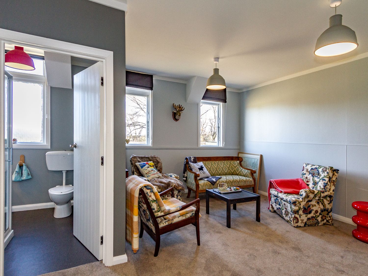 A living room with patterned chairs a small table and an open door showing a bathroom at Ohakune Barracks Ohakune