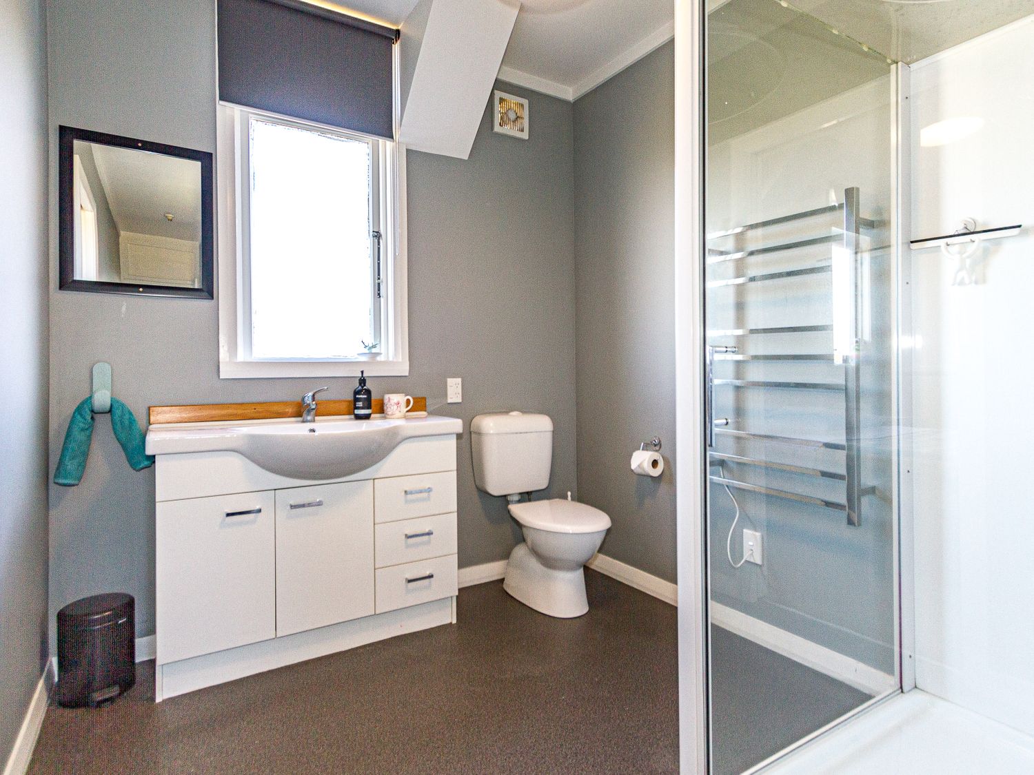 A bathroom with a sink cabinet under a window a toilet a glass shower enclosure and a towel rail at Ohakune Barracks - Ohakune Holiday Home in Ohakune