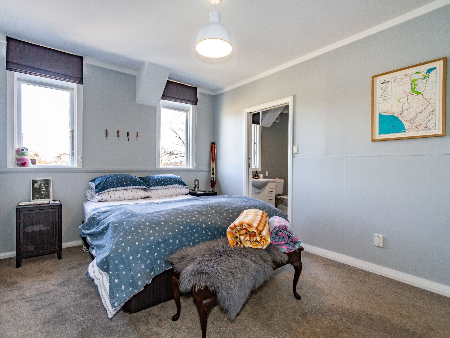 A bedroom with a bed, two windows, a bench with blankets, and an open door to a bathroom at Ohakune Barracks Ohakune