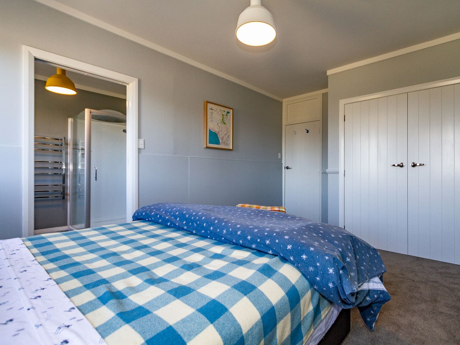 A bedroom with a bed covered with blue and white blankets a door leading to a bathroom and white closets at Ohakune Barracks Ohakune