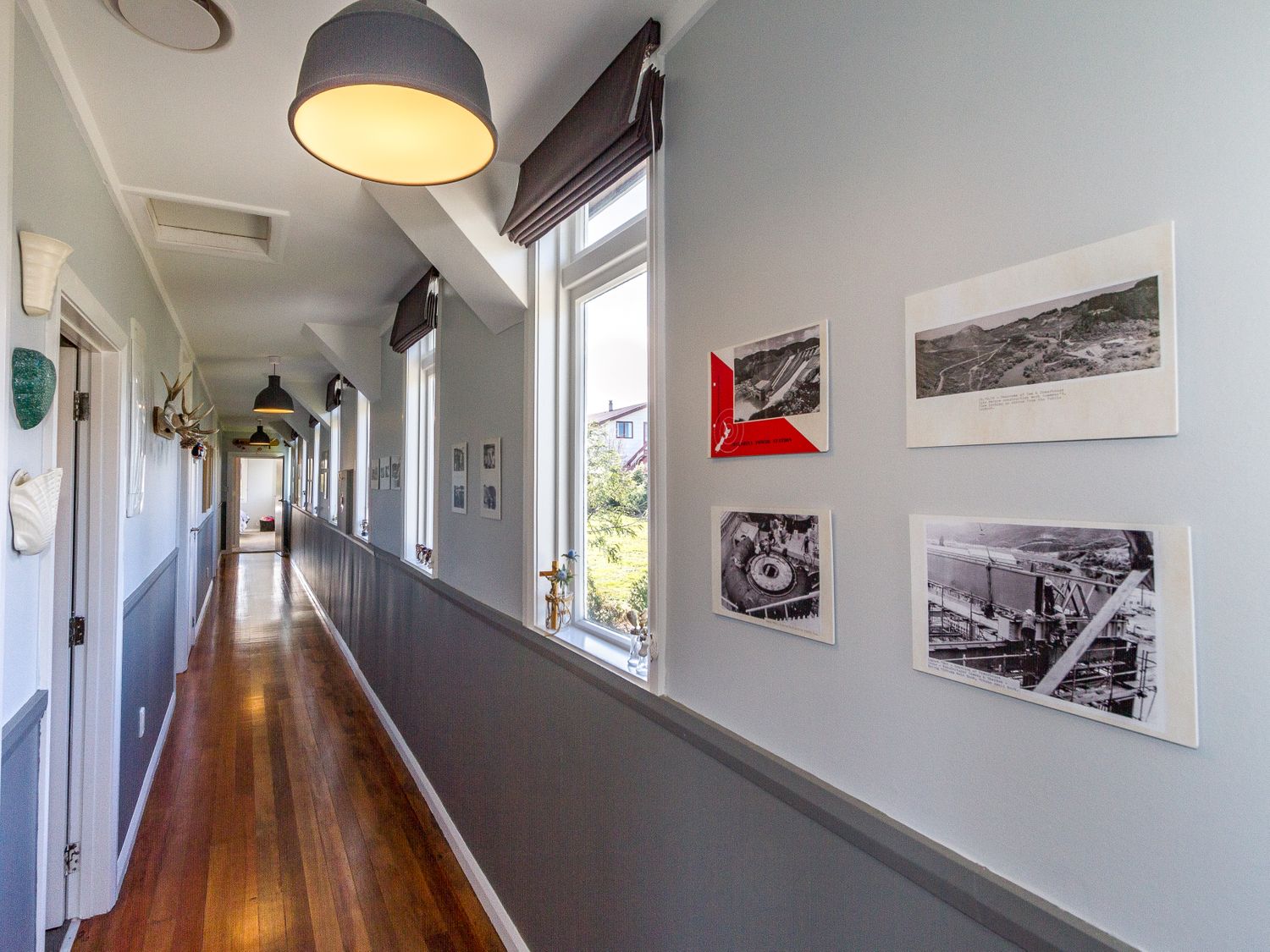 A hallway with wooden floor windows on one side and framed pictures on the wall at Ohakune Barracks in Ohakune