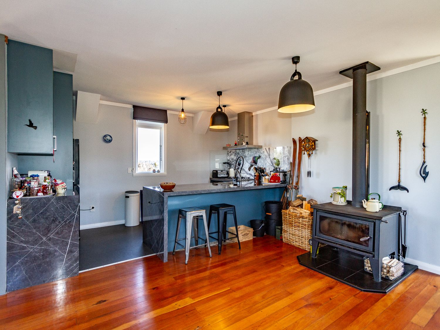 A kitchen with gray cabinets a marble island and a wood stove with hanging utensils at Ohakune Barracks Ohakune