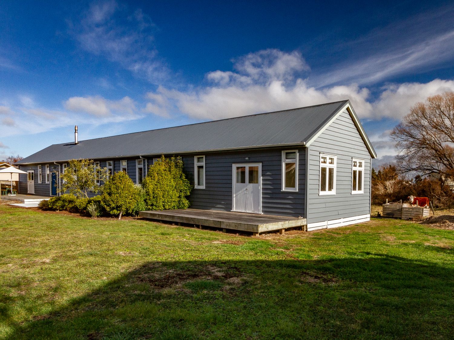 A long gray building with multiple windows and a small wooden deck in a grassy area at Ohakune Barracks Ohakune