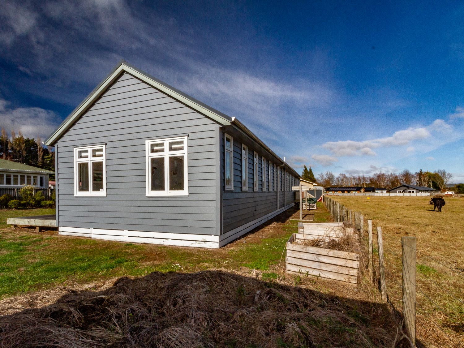 A long grey building with multiple windows next to a fenced field with a cow at Ohakune Barracks Ohakune