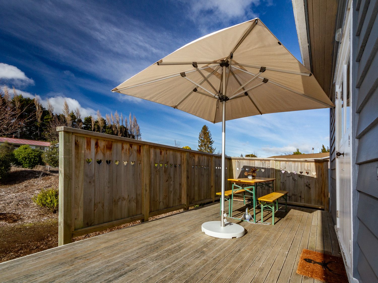 An outdoor wooden deck with a table and benches under a large umbrella at Ohakune Barracks Ohakune
