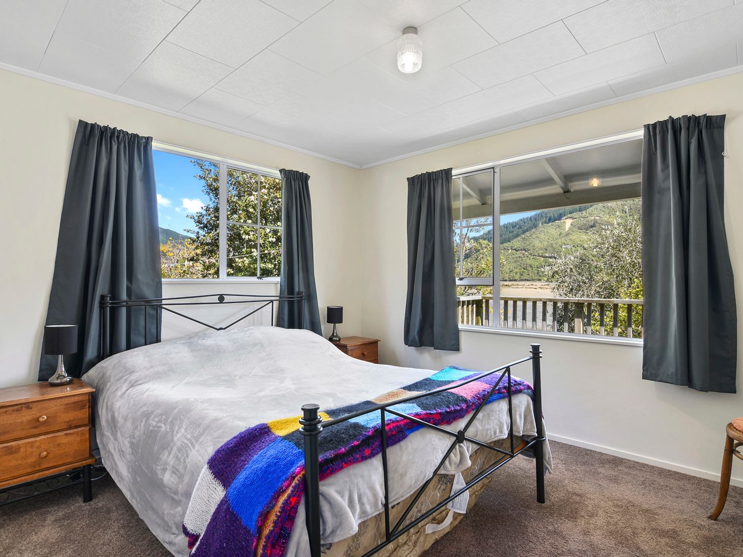 A bedroom with a bed covered in a blanket and two nightstands with lamps at Millard House - Marlborough Sounds