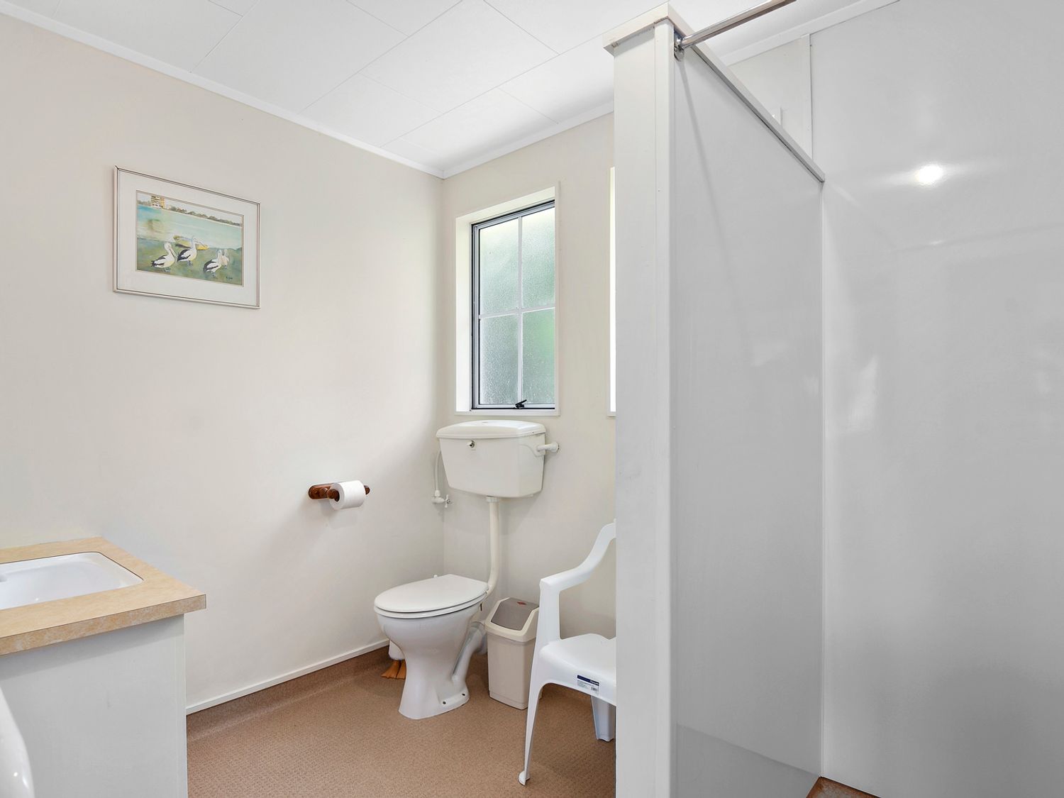 A bathroom with a toilet sink mirror shower and a plastic chair at Millard House - Marlborough Sounds