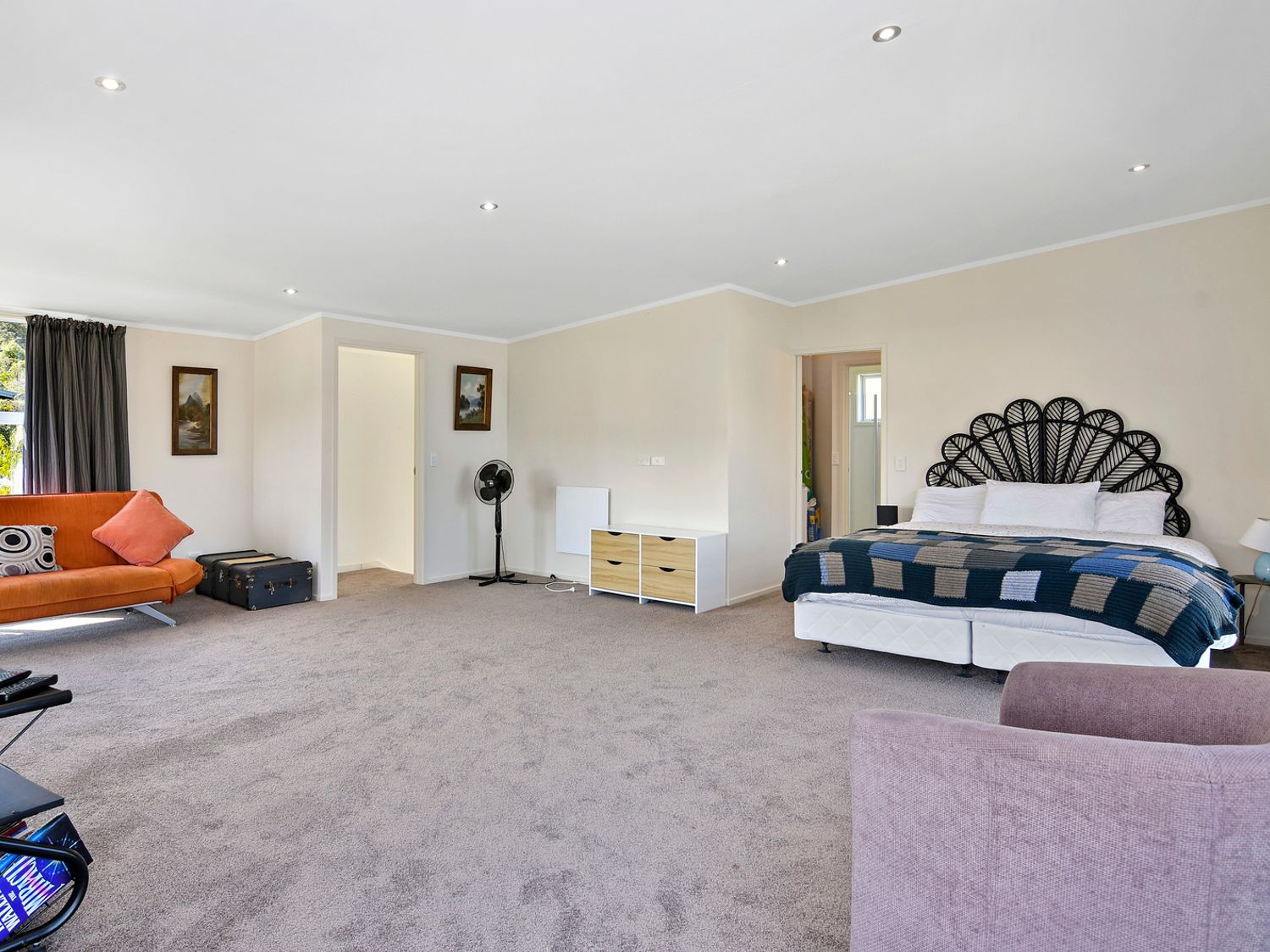 A bedroom with a bed a sofa a chair two paintings and a fan at Millard House - Marlborough Sounds