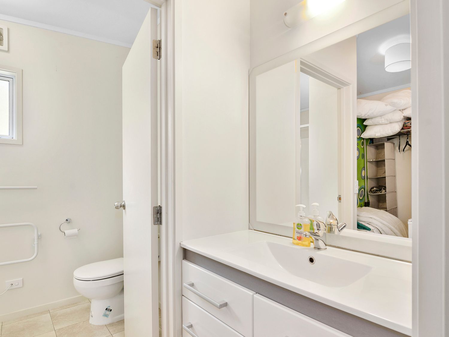 A bathroom with a white toilet a sink with a faucet a mirror and soap dispensers at Millard House - Marlborough Sounds